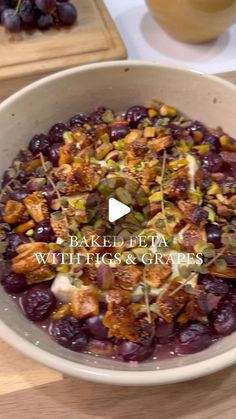 a bowl filled with grapes and nuts on top of a wooden table next to a cutting board