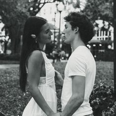 a man and woman standing next to each other in the grass with trees behind them