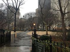 an empty street in the middle of a city with tall buildings and trees on both sides