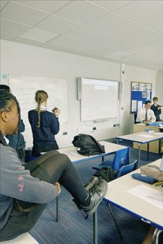 a group of people sitting at desks in front of a whiteboard and projector screen