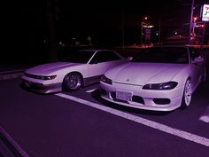 two white sports cars parked next to each other in a parking lot at night time