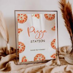 a pizza station sign sitting on top of a bed next to a vase with feathers