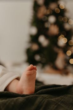 a baby laying on top of a bed next to a christmas tree with lights in the background