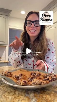 a woman with glasses is pointing at a plate of food on the counter top in front of her