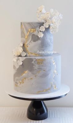 a three tiered cake with white flowers on top and gold leaf decoration around the edges