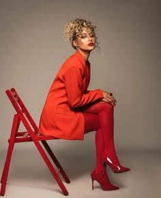 a woman sitting on top of a red chair wearing high heeled shoes and an orange coat