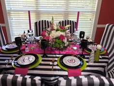 the table is set with black and white striped cloths, green plates, pink napkins, and flowers