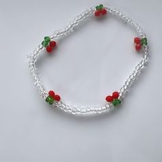 a white beaded bracelet with red, green and silver beads is shown on a white surface