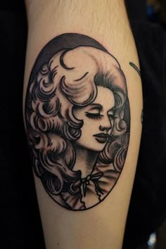 a woman's face with curly hair in a circle tattoo on the left thigh