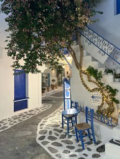 two blue chairs sitting under a tree in front of a white building with steps leading up to it