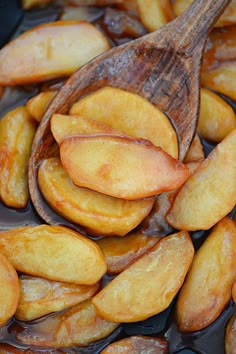 a wooden spoon filled with brown liquid next to sliced peaches on top of a table