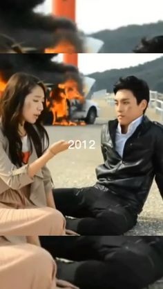 two people sitting on the ground in front of a fire