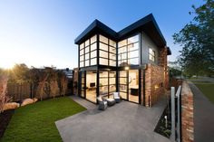 a modern house with large glass windows on the front and side walls, overlooking a grassy yard