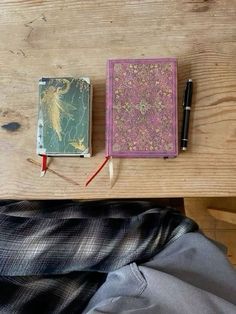 two notebooks are sitting on a wooden table next to a pen and pencil holder