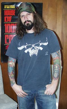 a man with long hair and tattoos standing in front of a poster