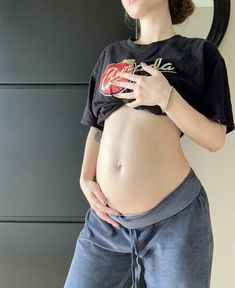 a pregnant woman wearing sweat pants and a t - shirt is posing for the camera