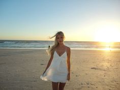 a woman standing on top of a sandy beach next to the ocean with her hair blowing in the wind