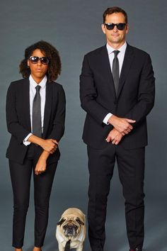 a man and woman standing next to a pug dog in front of a gray background