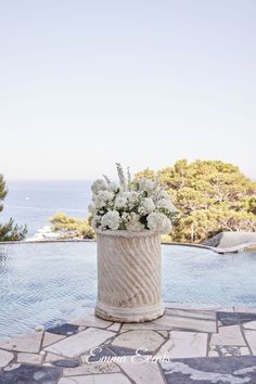 a vase with flowers sitting on top of a stone floor next to a swimming pool