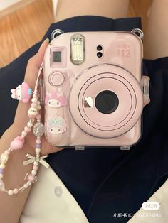 a person holding a pink camera with hello kitty charms on it's wrist and necklace