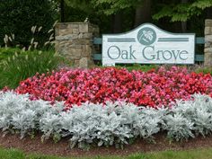 a sign for oak grove with flowers in front of it and bushes around the entrance