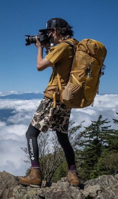 a man with a camera is standing on top of a mountain looking at the clouds