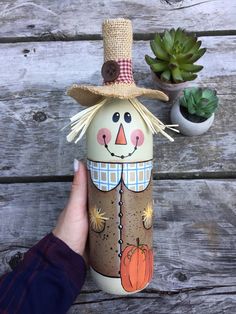 a hand holding up a painted bottle with a scarecrow on it and succulents in the background