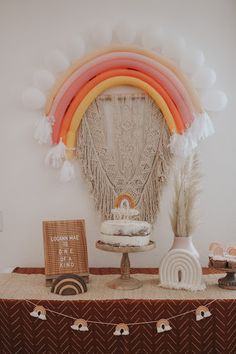 a table topped with a cake next to a rainbow shaped wall hanging on the wall