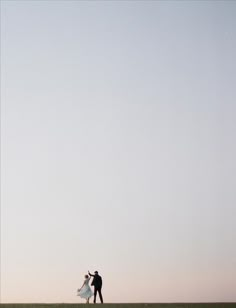 a man and woman standing on top of a lush green field under a blue sky