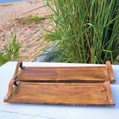 a wooden tray sitting on top of a white table next to tall grass and water