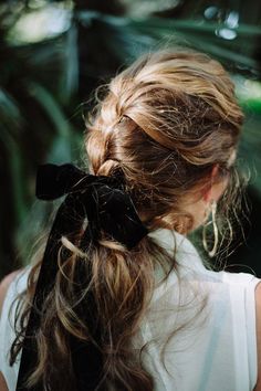 a woman with long hair wearing a black bow in her hair, looking down at the ground