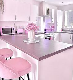 a pink kitchen with two stools and a center island that has flowers on it