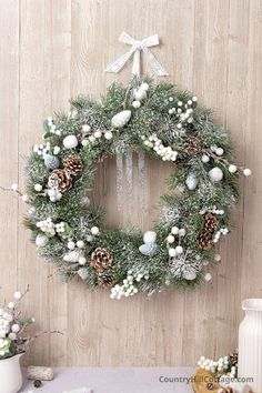 a christmas wreath hanging on the wall with pine cones and white balls around it,