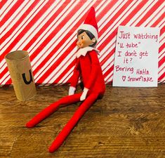 an elf is sitting on the floor next to a paper cup and a sign that says just watching you tube got it