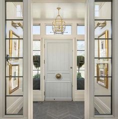 an open door leading to another room with two windows and a chandelier hanging from the ceiling