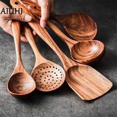 four wooden spoons with holes in them on a gray surface, one being held by someone's hand