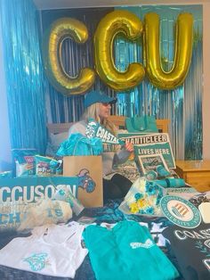 a woman sitting on top of a bed surrounded by blue and gold balloons in the shape of letters