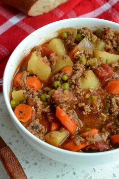 a white bowl filled with meat and vegetables on top of a red checkered table cloth