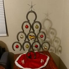 a christmas tree with ornaments on it and a cat bed under the base is sitting on a table