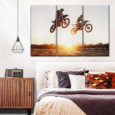 two motorcyclists jumping over a bed with the sun setting in the background