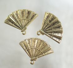 three small gold fan charms on a white surface