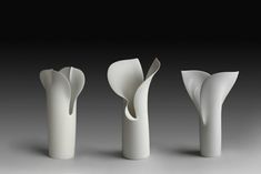 three white vases sitting next to each other on a gray surface with black background