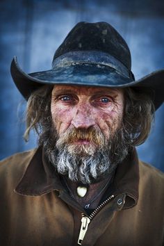 an old man wearing a hat and jacket with long hair is looking at the camera