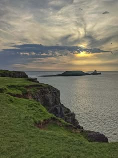 the sun is setting over an island in the ocean with green grass on both sides