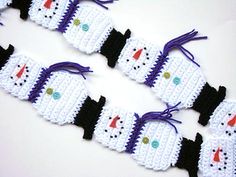 crocheted snowmen are lined up on a white surface with purple and black ribbons