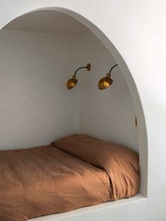 a bed sitting under two lamps in a bedroom next to a white wall and floor