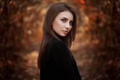 a woman with long brown hair and blue eyes posing for a photo in the woods