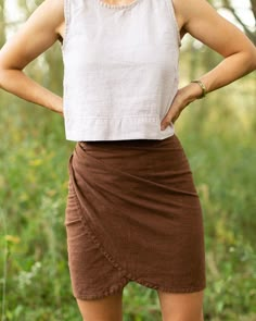 a woman standing in the woods with her hands on her hips wearing a white top and brown skirt