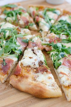 a pizza that is cut into slices on a wooden cutting board with greens and other toppings