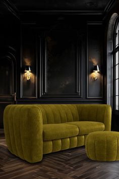 a green couch and ottoman in a dark room with black walls, wood flooring and large windows